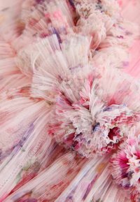Roosa tülli kangas, millel on kogutud, volangidega osad, millel on pastellsetes värvides peened lillemustrid. Pehme tekstuur ja delikaatsed kihid on nähtavad.