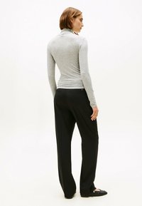 Grauer Langarm-Turtleneck mit einer figurbetonten Passform und glatter Textur, kombiniert mit schwarzen weit geschnittenen Hosen und flachen Schuhen.