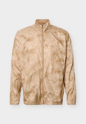 Μπεζ ζακέτα με φερμουάρ και σχέδιο tie-dye, με ψηλό γιακά, μακριά μανίκια και ελαστικά μανσέτα, απλωμένη επίπεδη σε λευκό φόντο.