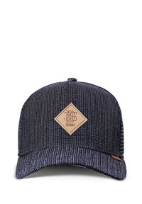 Baseball cap with a dark blue textured fabric design, featuring a tan leather diamond patch with logo and a slightly curved brim.