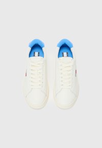Hvite lær sneakers med en lys blå polstret krage, hvite lisser og en rød og blå logo på siden. Glatt tekstur og avrundet form.