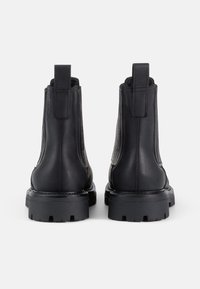 Botas de cuero negro hasta el tobillo con suelas planas y paneles laterales texturizados. Presentan una lengüeta y un acabado suave, diseñadas para la durabilidad.