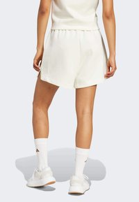 Biele fleecové šortky s elastickým pásom a bočnými rozparkami. Skombinované s bielymi teniskami a bielymi ponožkami s hnedým logom.