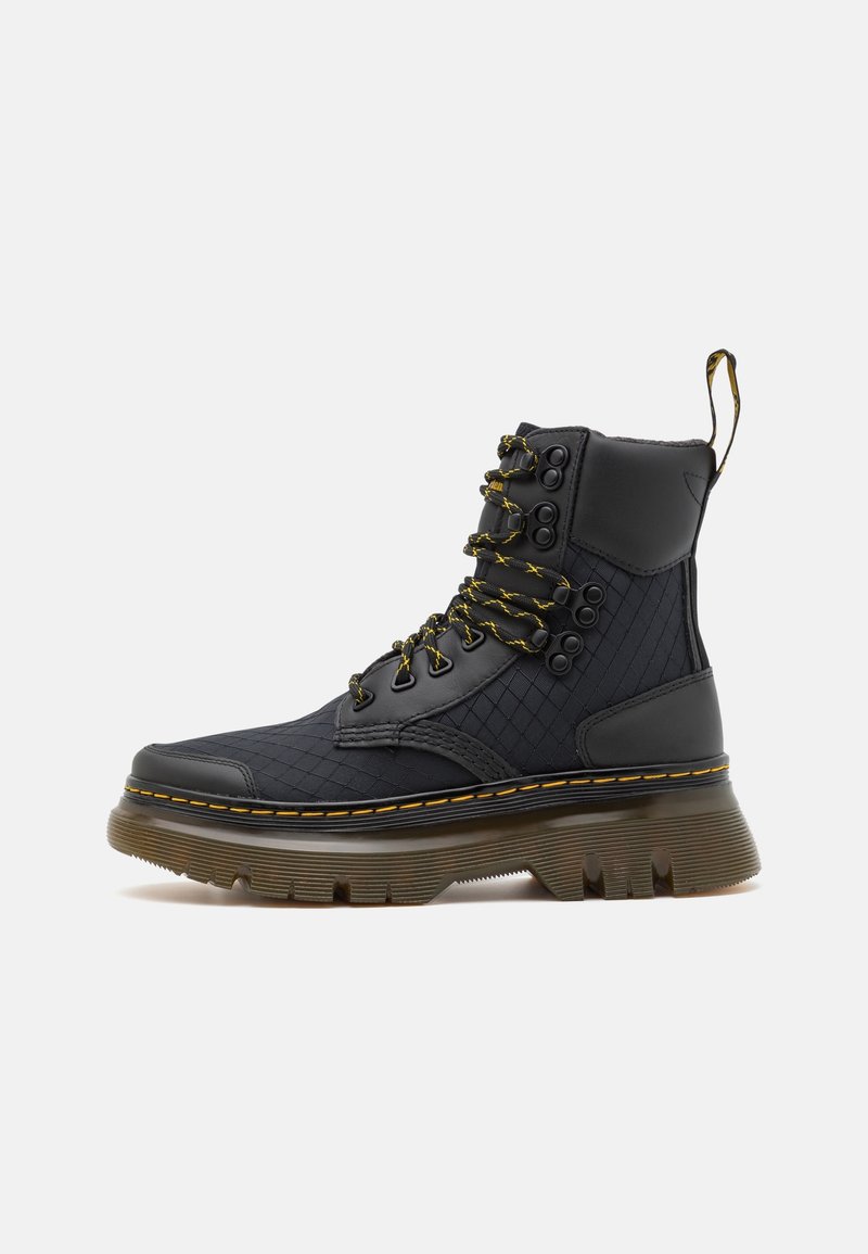 Botte montante noire avec semelle épaisse marron, coutures jaunes, côtés en tissu matelassé, lacets noirs et jaunes, et languette à l'arrière.
