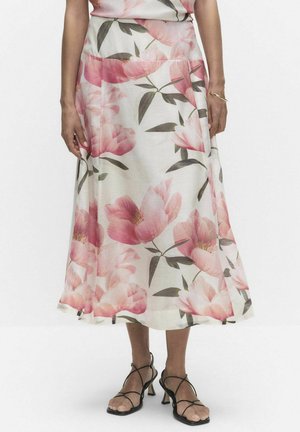 Kvinde iført hvid midi-nederdel med stort rosa blomsterprint, stylet med sorte stropper højhælede sko og et guldbånd omkring højre håndled.