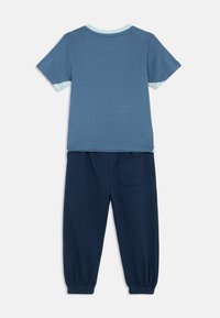 Blauw kortmouwen overhemd met lichtblauwe binnenmanchetten, gecombineerd met donkerblauwe elastische cuff broek met een achterzak, plat gelegd.