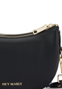 Zwarte leren schoudertas met een gebogen vorm, gouden hardware, dubbele ritsluiting en een logo in reliëf aan de voorkant.