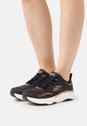 Zapatillas deportivas negras con una parte superior de punto texturizado, detalles en beige, suela acolchada y cordones negros. Logo visible en el lateral.