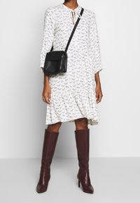 Vit långärmad klänning med svart djurmönster, lös passform, volangkant, matchad med en svart axelremsväska och bordeauxfärgade knähöga stövlar.