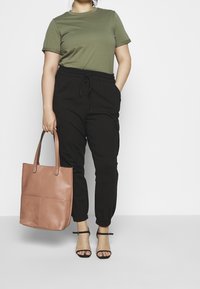 Oliwkowa bawełniana koszulka, czarne tapered joggery z kieszeniami, różowa skórzana torba, czarne sandały na obcasie z paskami.