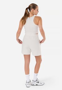 White ribbed tank top paired with high-waisted, soft fabric shorts. Model wears white sneakers and ankle-length white socks. Plain, minimalist design.