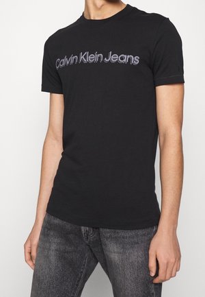 Czarna bawełniana koszulka z napisem „Calvin Klein Jeans” w fioletowym kolorze. Krótkie rękawy, okrągły dekolt, dopasowany krój i gładka faktura.