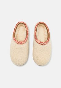 Cremefarvede slippers med en fluffy tekstur, prydet med en rød og cremefarvet dekoration omkring åbningen og et blødt indvendigt foret.