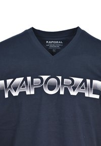 Námořnická modrá tričko s výstřihem do V vyrobené z bavlny s velkým bílým texturovaným logem "KAPORAL" přes přední část, které má gradientní tečkovaný vzor.