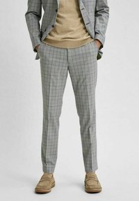 Šedé kostkované kalhoty slim fit, vyrobené z texturované tkaniny s modrými a zelenými liniemi. V kombinaci s béžovým svetr a světlými botami.