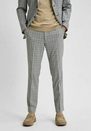 Szare spodnie w kratę o slim fit, wykonane z teksturowanej tkaniny z niebieskimi i zielonymi liniami. Połączone z beżowym swetrem i jasnym obuwiem.