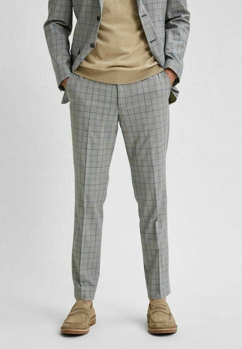 Šedé kostkované kalhoty slim fit, vyrobené z texturované tkaniny s modrými a zelenými liniemi. V kombinaci s béžovým svetr a světlými botami.