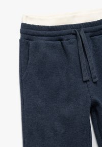 Marineblaue Jogginghosen aus strukturiertem Stoff mit geripptem Finish, ausgestattet mit einem elastischen Taillenbund und Kordelzug sowie seitlichen Taschen.