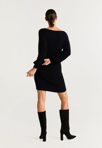 Robe en maille côtelée noire avec une silhouette ajustée et des manches longues, associée à des bottes noires à talons montant jusqu'aux genoux. Design simple et élégant.