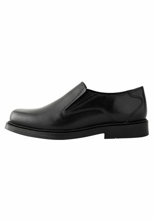 Chaussure en cuir noir à enfiler avec un bout arrondi, un petit talon, des panneaux latéraux élastiques et une surface lisse. Présente des coutures décoratives et une semelle plate.
