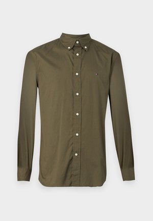 Chemise à manches longues de couleur vert olive avec des boutons blancs et un petit logo sur la poitrine gauche. Fabriquée en tissu lisse.