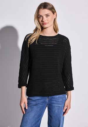Maglione nero a maglia con un design a strisce testurizzato, colletto rotondo e maniche a tre quarti. Abbinato a jeans in denim blu.