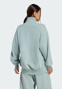 Svetlá azúrová oversized mikina s vysokým golierom a rebrovanými manžetami, s hladkou textúrou a spustenými ramennými švami.