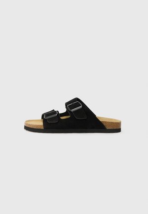 Zwarte suedine slide-sandaal met twee verstelbare gespen, kurken voetbed en rubberen zool; vlak ontwerp met minimalistische styling.