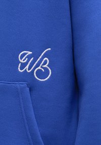 Modrá mikina s měkkou texturou a přední kapsou. Obsahuje bílé vyšívané logo. Hladká tkanina s rovnými švy.