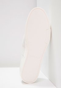 Vit sneaker med slätt läder och tygöverkännande, med en texturerad gummisula och svag "Calvin Klein" branding på sidan.