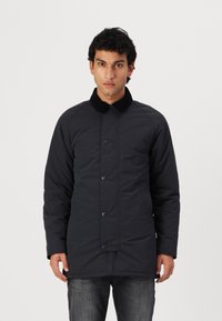Casaco acolchoado preto com um colarinho preto suave, apresentando um fecho frontal por botões e dois bolsos laterais. Textura suave e design de comprimento médio.