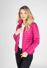 Giacca trapuntata puffa magenta con colletto alto, zip frontale e polsini elasticizzati, indossata sopra una camicia grigia chiara e pantaloni neri.