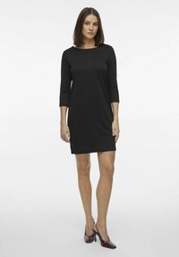 Svart, kortärmad klänning med rund hals och slim fit. Tillverkad av mjukt tyg, knälång, i kombination med mörka högklackade skor.