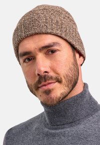 Beanie marrone a maglia con un motivo a coste texturizzato, abbinato a un maglione grigio a collo alto. Il berretto si adatta bene, coprendo le orecchie.