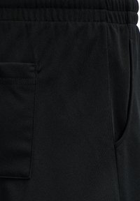 Gros plan sur un pantalon noir avec une ceinture élastique et des poches latérales et arrière visibles, en tissu doux.