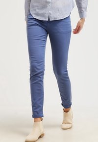 Pantalons slim-fit bleus en mélange de coton doux avec une texture lisse. Comprend des ourlets roulés et des poches latérales, associés à des bottines beige.