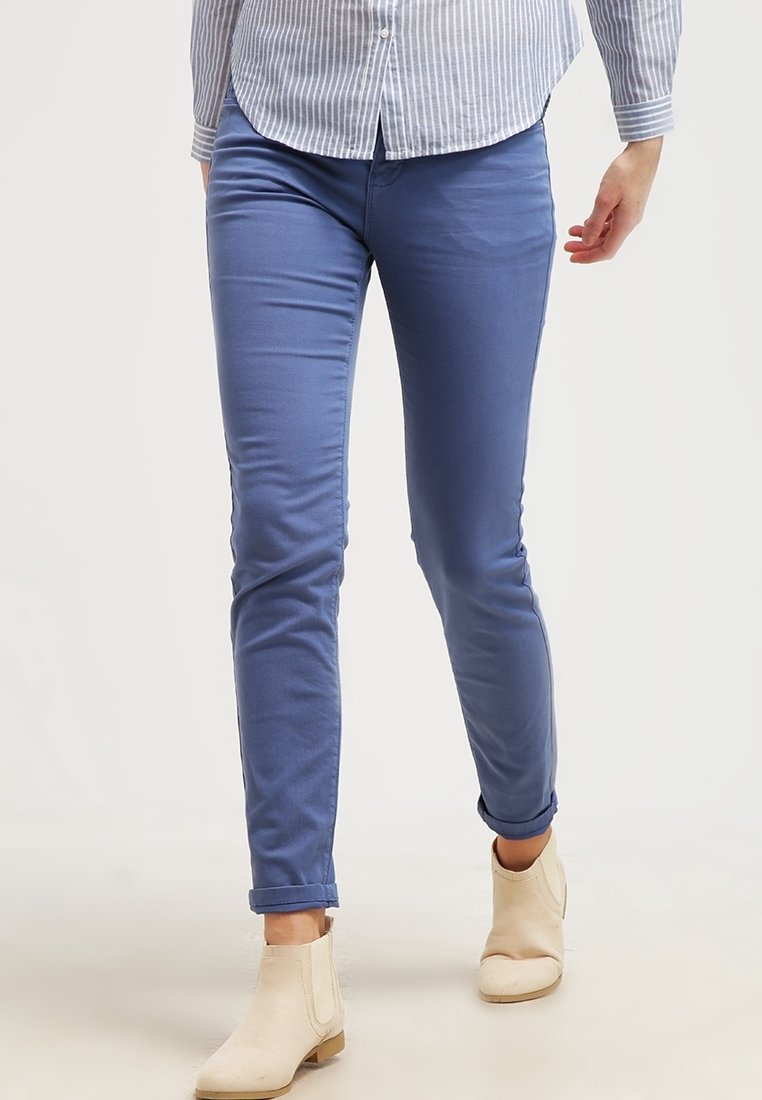 Pantalons slim-fit bleus en mélange de coton doux avec une texture lisse. Comprend des ourlets roulés et des poches latérales, associés à des bottines beige.