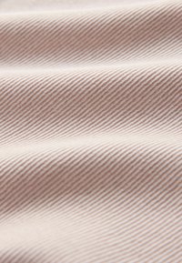 Mäkká tkanina s jemnou diagonálnou rebrovou textúrou v svetlobežových odtieňoch, zobrazujúca jemné záhyby a tiene.