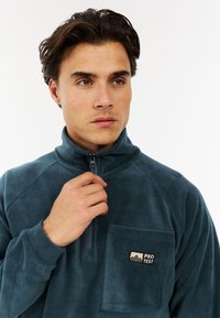 Sudadera de forro polar en azul oscuro, con cuello con cremallera, bolsillo en el pecho con logo y una textura suave. Adecuada para uso casual.