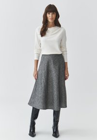 Sivá áčková midi sukňa skombinovan�á s bielym topom s cowl-neck a dlhým rukávom. Nosené s lesklými čiernymi čižmami po kolená.