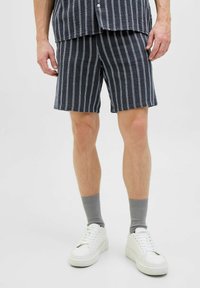 Mørkeblå og hvide stribede shorts lavet af letvægtsstof, med en elastisk talje. Parret med hvide sneakers og grå strømper.