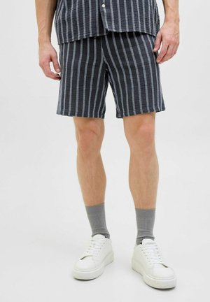 Mørkeblå og hvide stribede shorts lavet af letvægtsstof, med en elastisk talje. Parret med hvide sneakers og grå strømper.