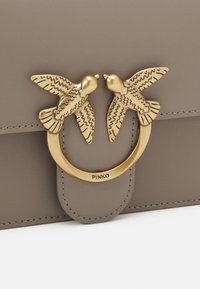 Borsa a tracolla grigia in pelle caratterizzata da un anello in tonalità oro con due decorazioni a forma di uccello. La borsa presenta dettagli di cucitura discreti e un design elegante.
