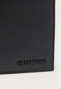 Close-up of black textured leather with stitching and embossed Valentino logo in the bottom right corner.