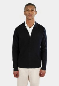 Marinblå zip-up tröja med krage och ribbade ärmslut. Tillverkad av texturerad stickad tyg, med en figurnära silhuett.