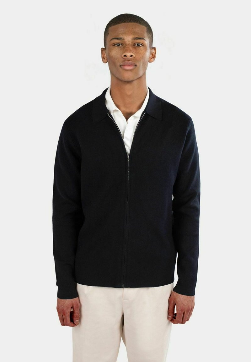 Marinblå zip-up tröja med krage och ribbade ärmslut. Tillverkad av texturerad stickad tyg, med en figurnära silhuett.