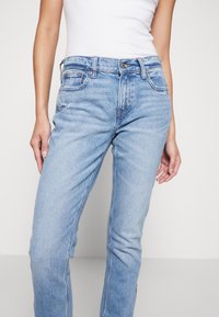 Vaqueros de denim azul claro con corte recto, que cuentan con bolsillos delanteros y traseros, un ligero desgaste y un diseño clásico de cinco bolsillos.