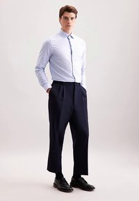 Camicia a quadri blu e bianca con colletto appuntito, abbinata a pantaloni larghi blu navy e scarpe eleganti nere. Design semplice e su misura.