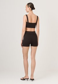 Barna bordázott kötött crop top széles pántokkal és passzoló magas derekú sorttal. A modellen fekete szandál van, ami minimalista dizájnt mutat be.