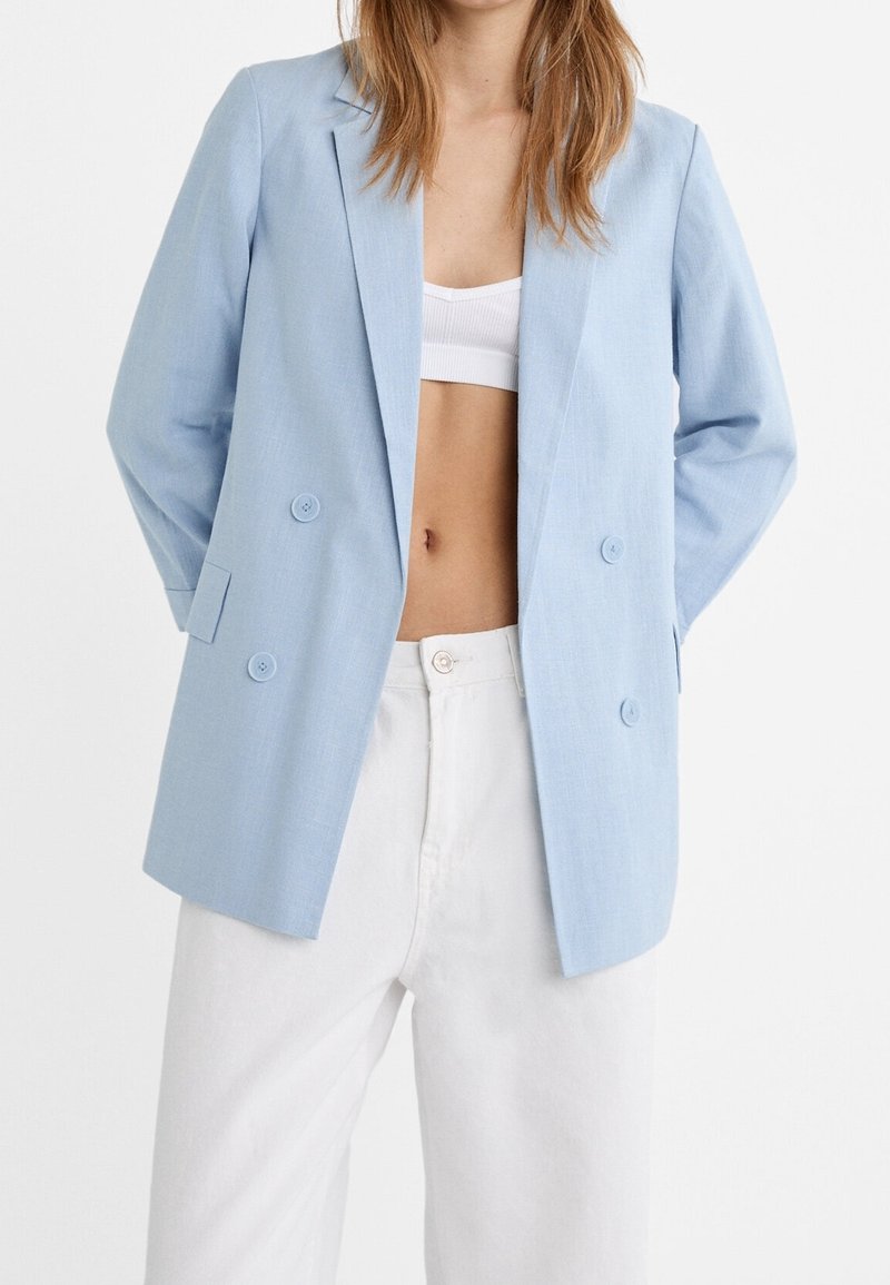 Blazer doppiopetto azzurro chiaro realizzato in tessuto testurizzato, con grandi bottoni e revers, abbinato a pantaloni bianchi a vita alta.
